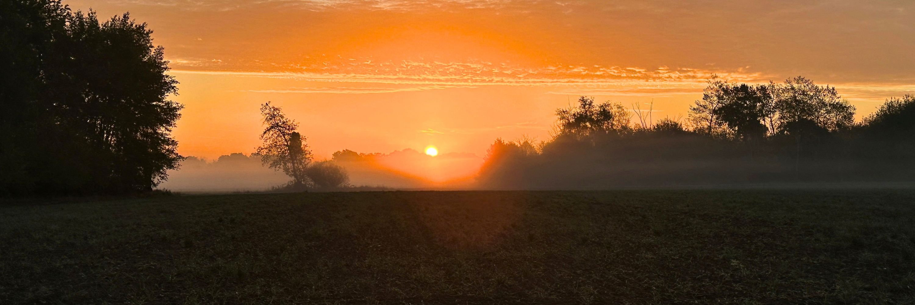 Oranger Sonnenaufgang über den nebligen Feldern um Rödermark, die in tiefem Schatten liegen