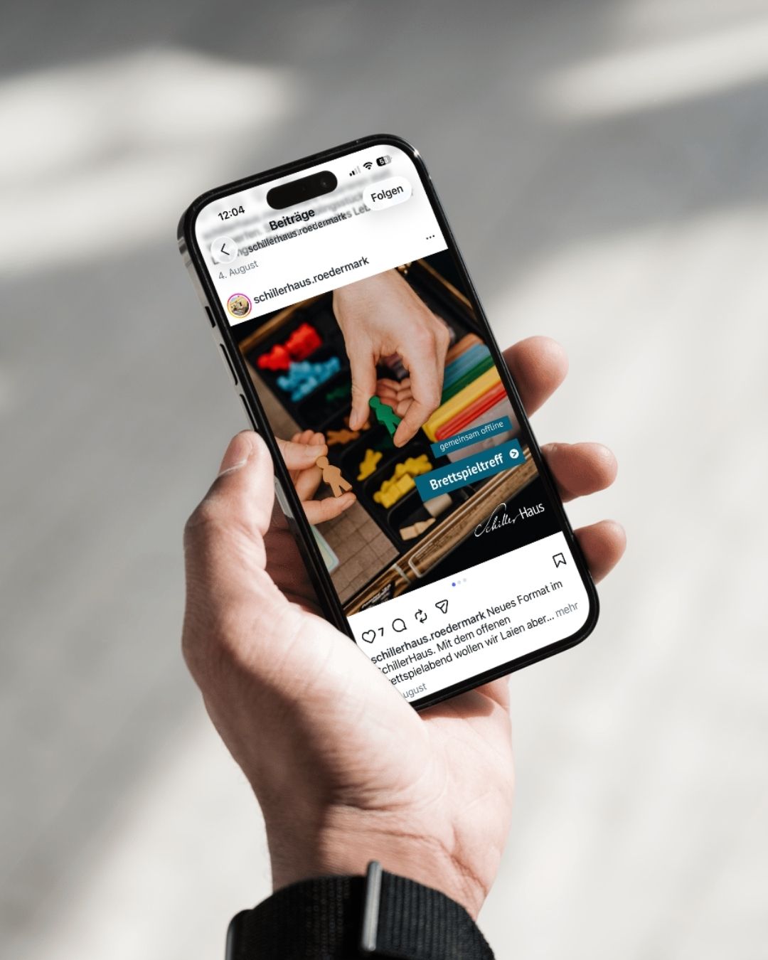 Eine Hand hält ein Smartphone, darauf sichtbar ist das Instagram-Profil des SchillerHaus Rödermark