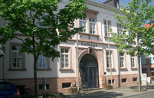 Alter Rathauseingang mit der Überschrift "Rathaus" des Rathaus in Ober-Roden, flankiert von zwei grün belaubten Bäumen.