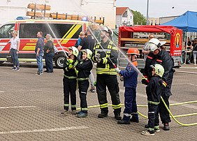 Kinder in Feuerwehausrüstung spritzen gemeinsam Wasser