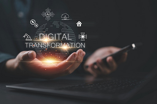 Hand über Laptop mit schwebender digitaler Weltkugel und den Worten 'DIGITAL TRANSFORMATION' sowie mehreren Technologie-Icons