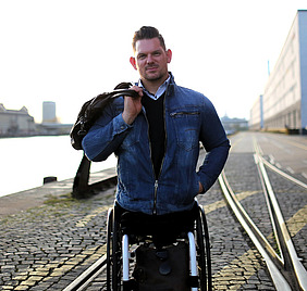 Florian Sitzmann mit blauer Jacke im Rollstuhl sitzend an einer Kaimauer.