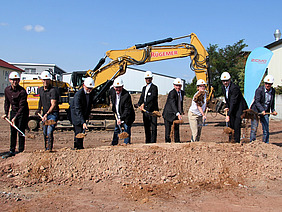 Spatenstich mit Ehrengästen, im Hintergrund ein Bagger