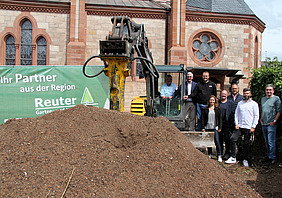 Akteuere stehen neben einem Bagger und Erdaushub vor der Kirche St. Nazarius