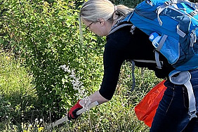 Frau mit Handschuhen, Ruckdack und roter Mülltüte beim Müllsammeln.