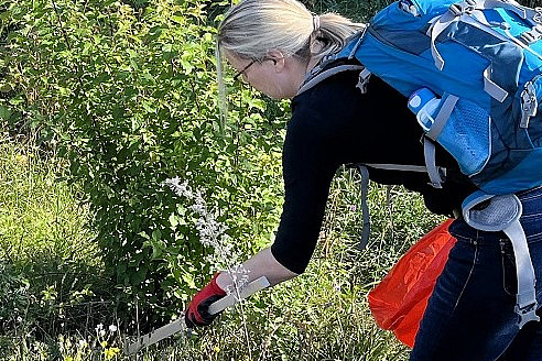 Frau mit Handschuhen, Ruckdack und roter Mülltüte beim Müllsammeln.